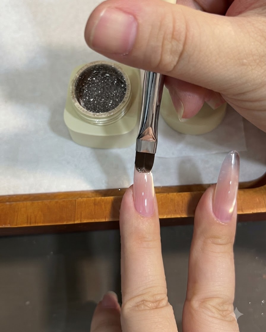 Ein flacher Pinsel trägt funkelndes braunes Glittergel auf die Nagelspitze eines Mandelnagels auf und zieht es für einen Ombré-Effekt nach unten.
