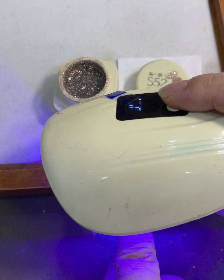 Ein Finger mit einem Glitter-Verlaufs-Nagel härtet unter einer kleinen tragbaren UV- und LED-Nagellampe aus.