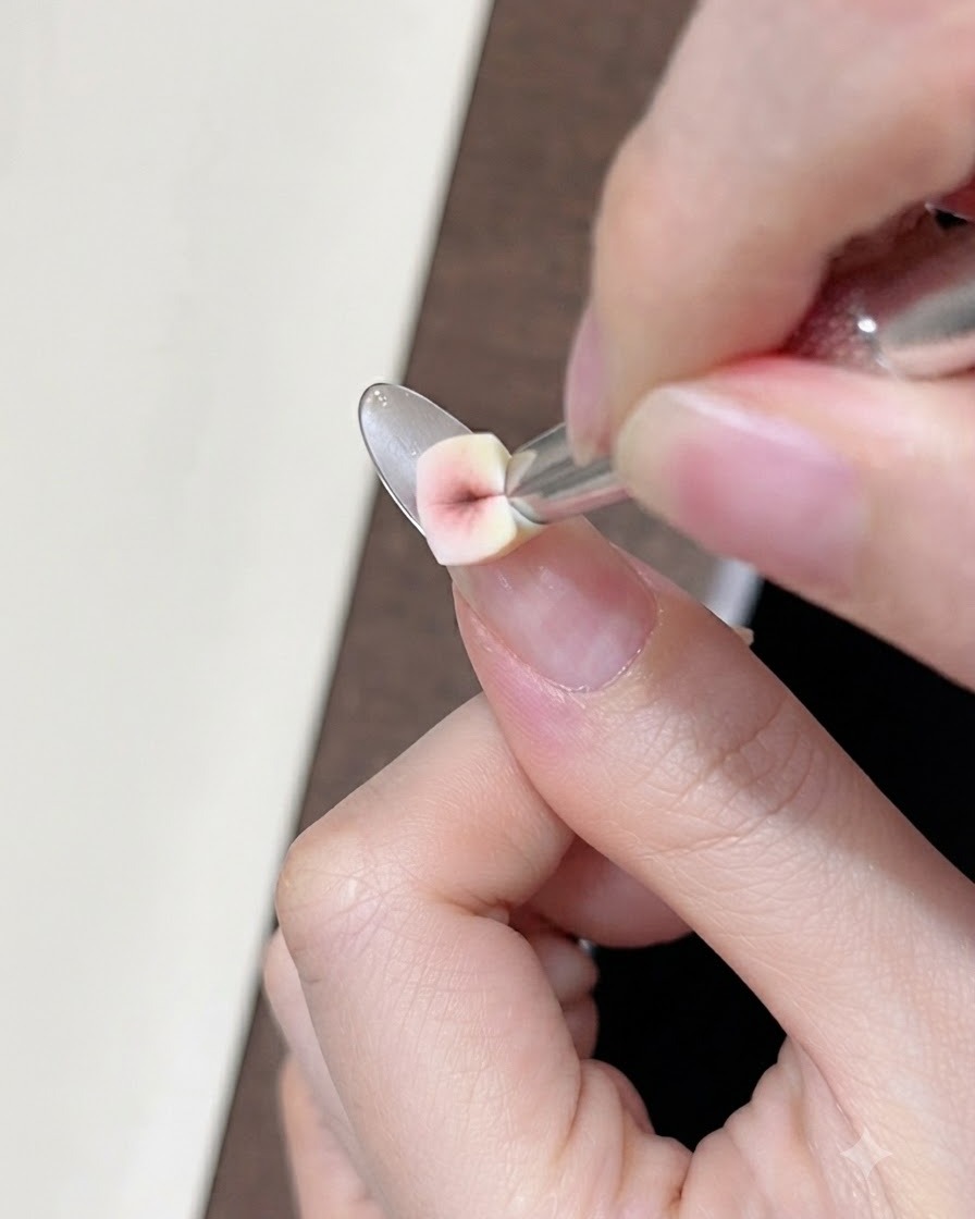 Eine Nahaufnahme eines kleinen Schwamms, der nudefarbenes Concealer-Gel auf den Naturnagel nahe der Smile-Line tupft.