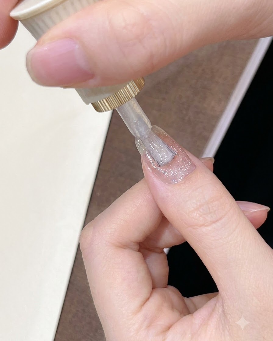 Ein Pinsel trägt einen durchscheinenden, leuchtend pink-braunen Gel-Nagellack auf die Oberfläche eines manikürten Nagels auf.