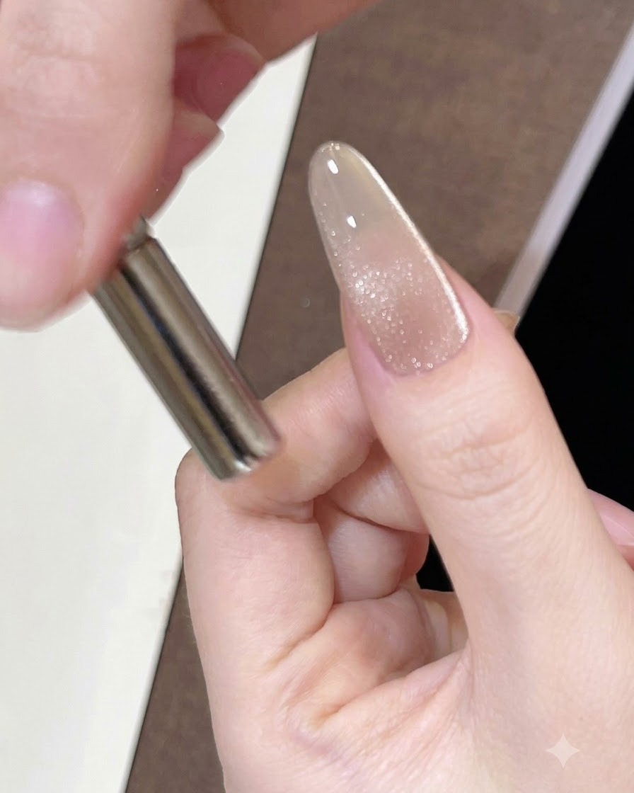 Ein zylindrischer Magnet wird dicht an die Seite eines lackierten Nagels gehalten, um den magnetischen Schimmer zu bewegen.