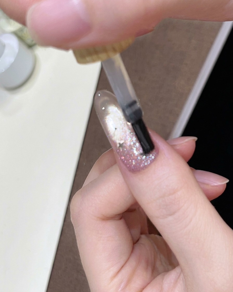 Ein Pinsel trägt einen glänzenden klaren Top Coat über den verzierten Ombré-Nagel auf.