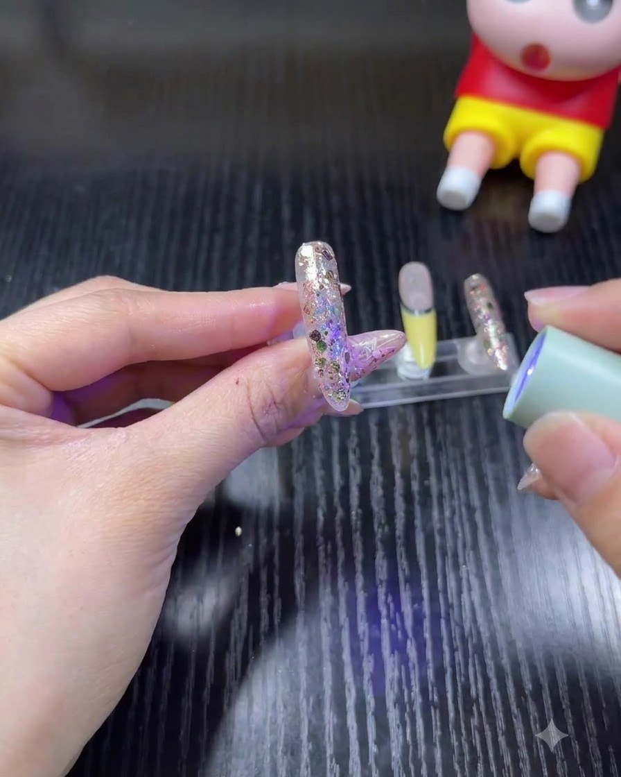 Eine Hand hält eine kleine, tragbare UV-/LED-Lampe über einen glitzernden Nagel, um das Gel auszuhärten.