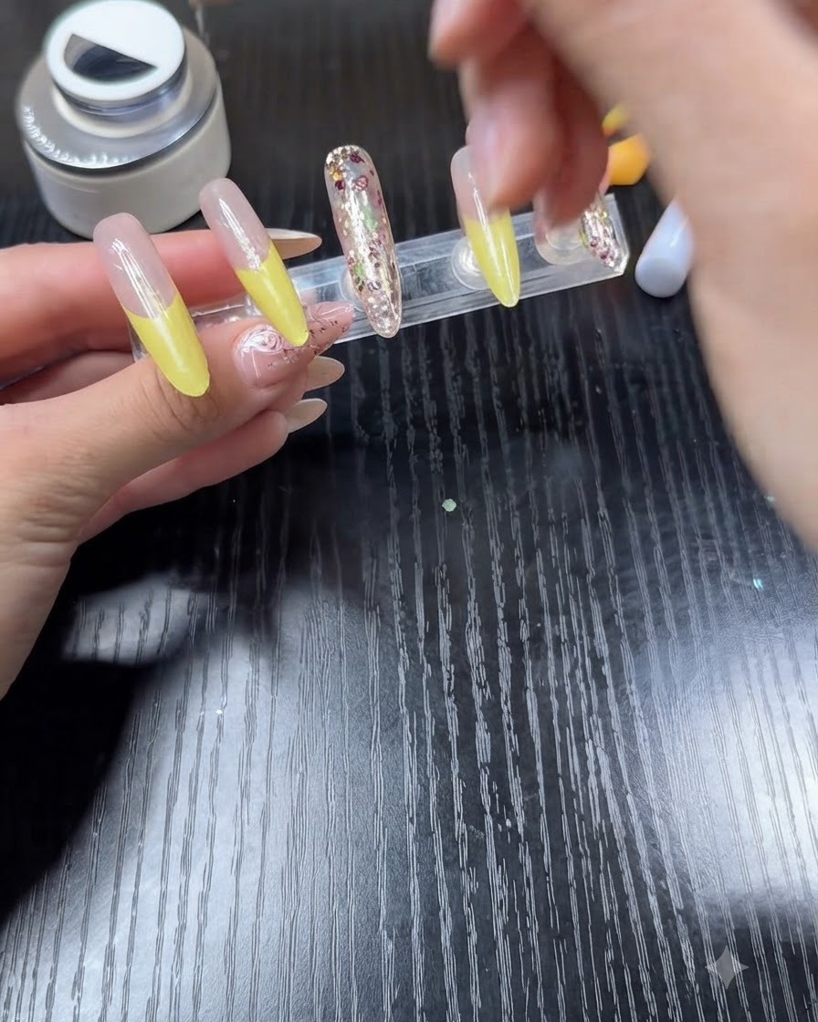 Ein Nagellackpinsel trägt klaren Überlack auf einen Nagel mit leuchtend gelber French Tip auf.
