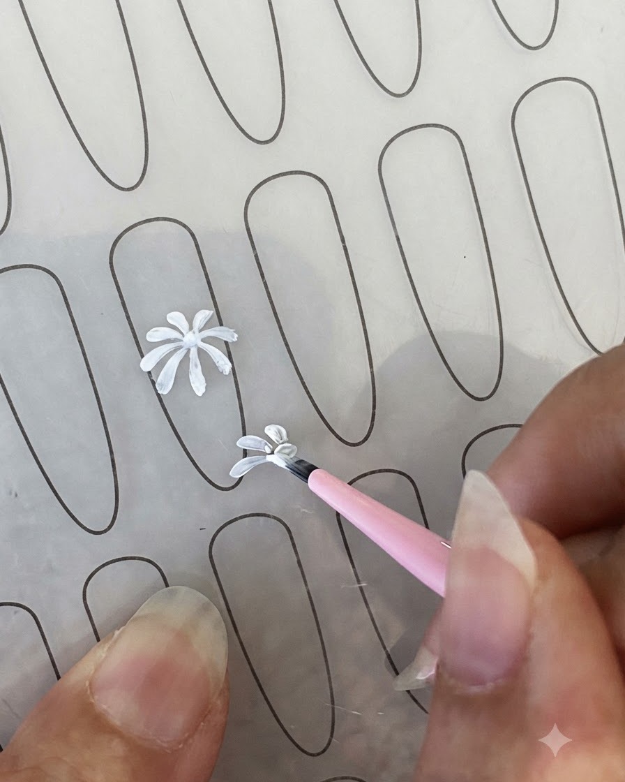 Ein fertiger weißer Gänseblümchen-Blütenblattumriss auf einem Nagel-Übungsblatt neben einem feinen Liner-Pinsel.