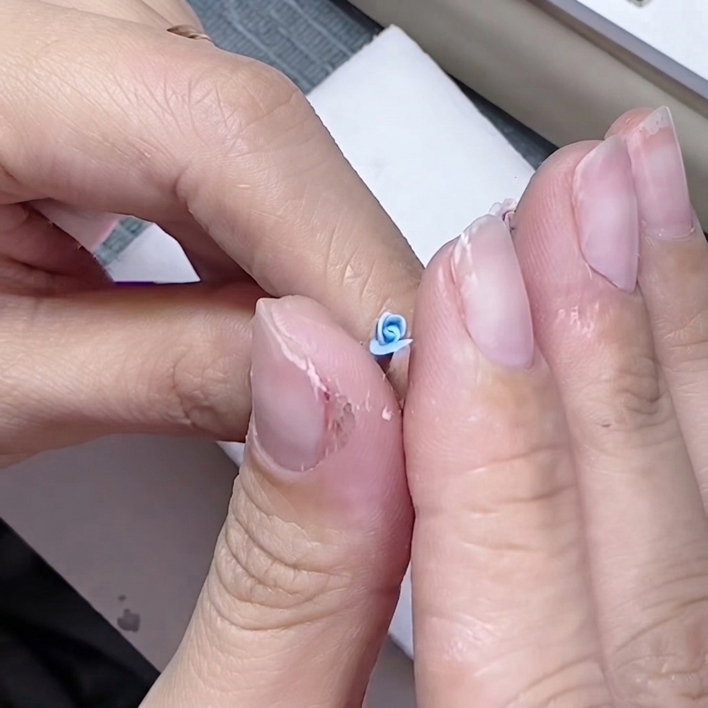Finger knifen feinfühlig die Basis eines kleinen blauen Blütenblatts um den Rosenkern.