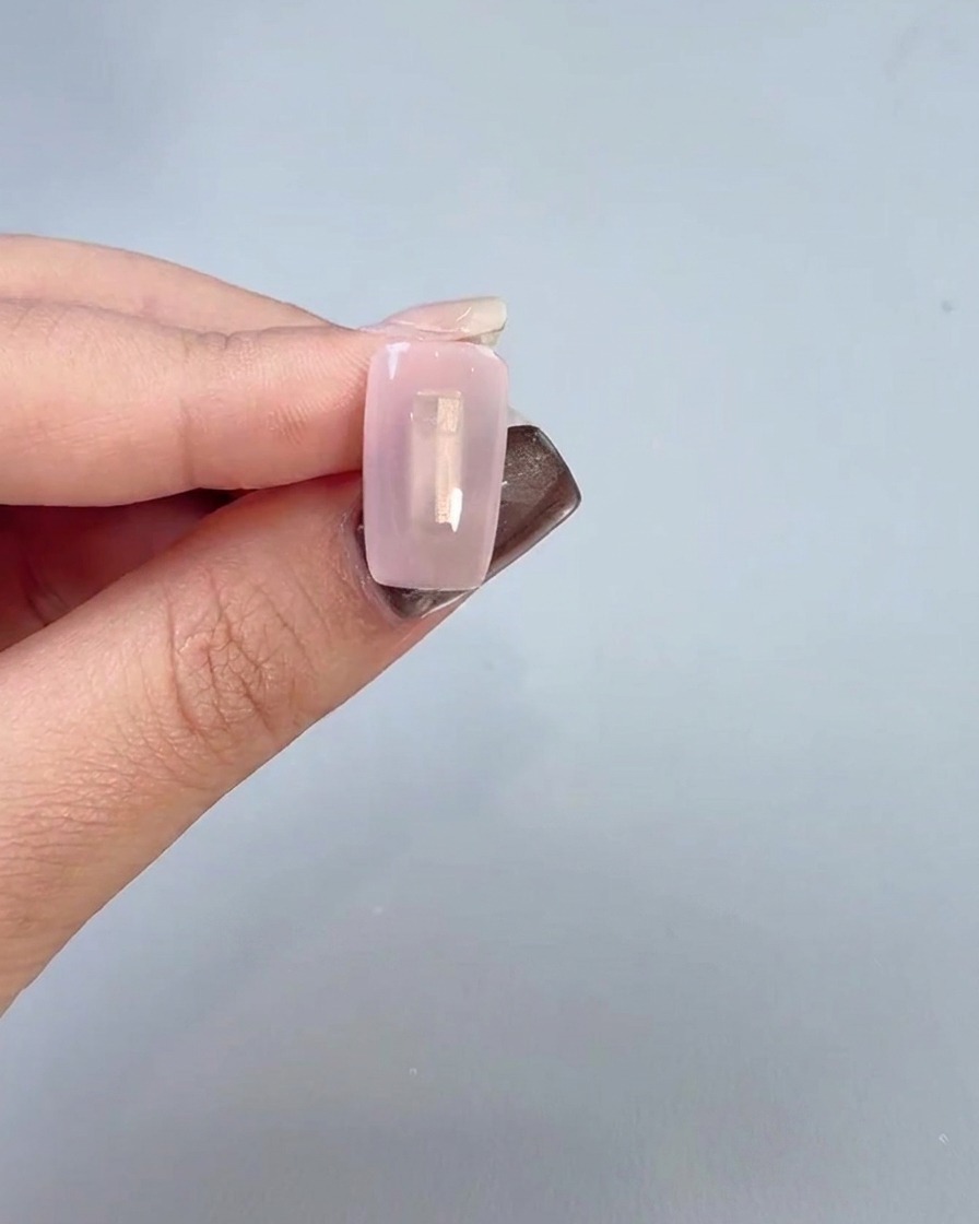 Eine Nahaufnahme einer Hand, die einen klaren Basislack-Gels mit einem Pinsel auf eine Nageloberfläche aufträgt.
