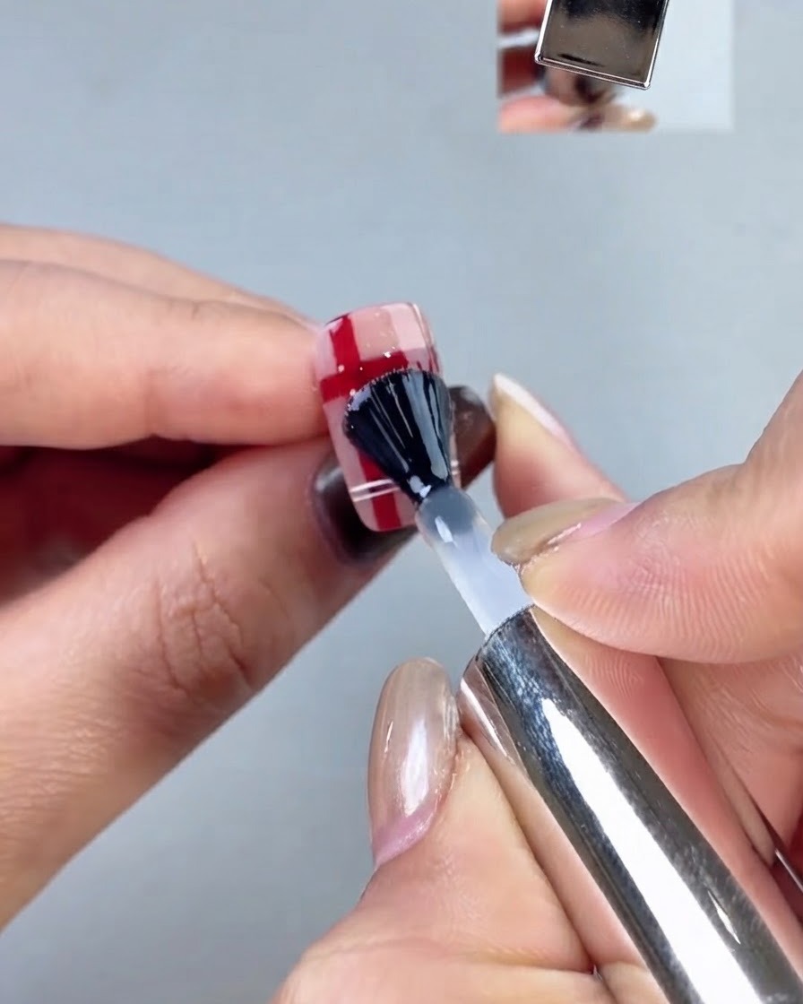 Ein schwarz kapselnder Nagelpinsel trägt eine klare Top-Coat-Schicht über ein Karomuster-Nageldesign auf.