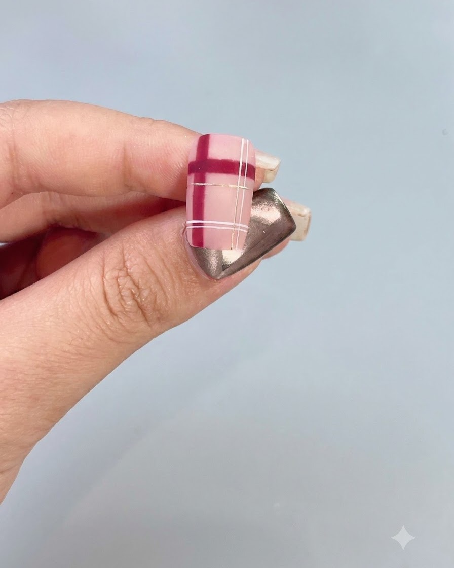 Eine Nahaufnahme eines dekorierten Nagels mit rot-weißem Karomuster und Goldakzenten.