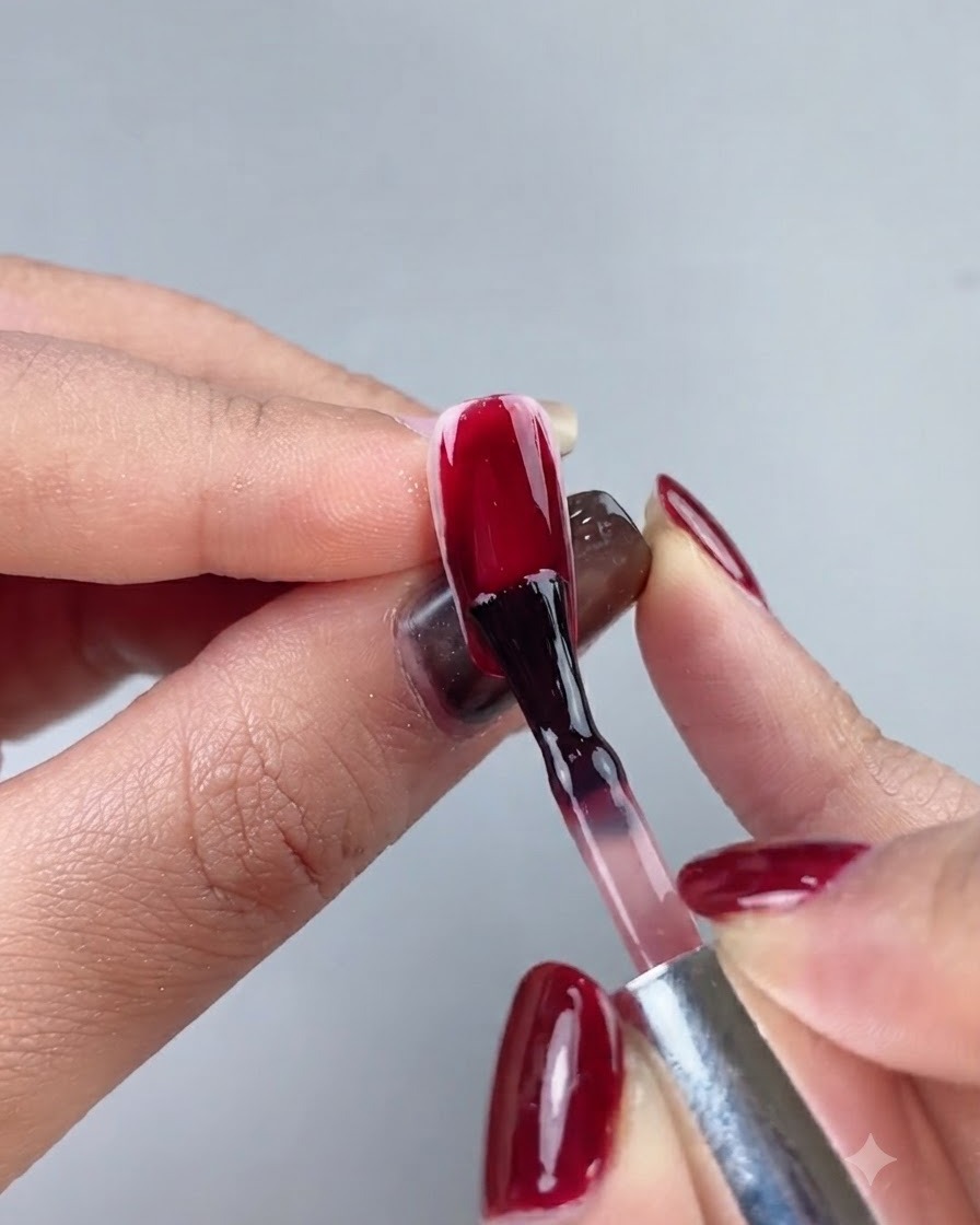 Ein Nagelpinsel trägt tiefes oxblutrotes Gel-Polish auf eine vollständige Nagelverlängerung auf.
