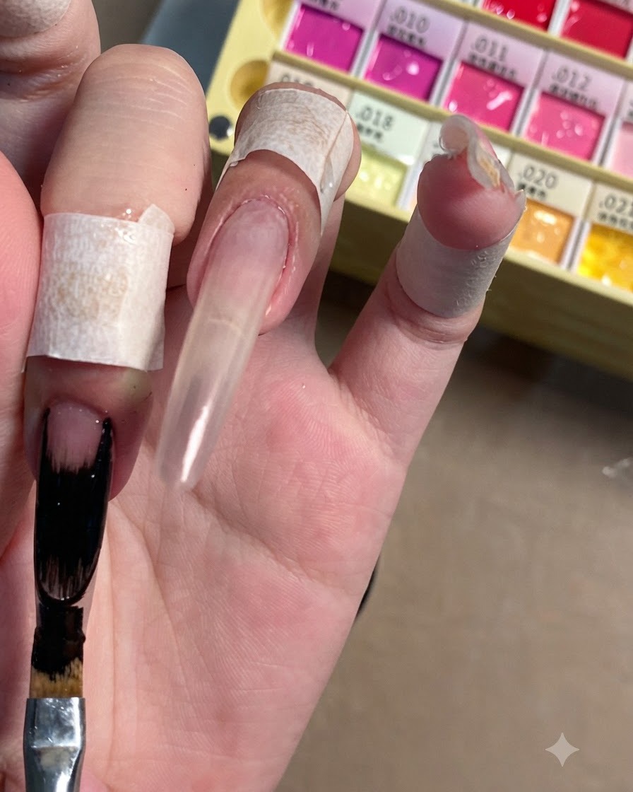 Ein flacher Nail-Art-Pinsel trägt undurchsichtiges schwarzes Gel-Polish auf die verlängerte Spitze eines klaren Stiletto-Nagels auf.