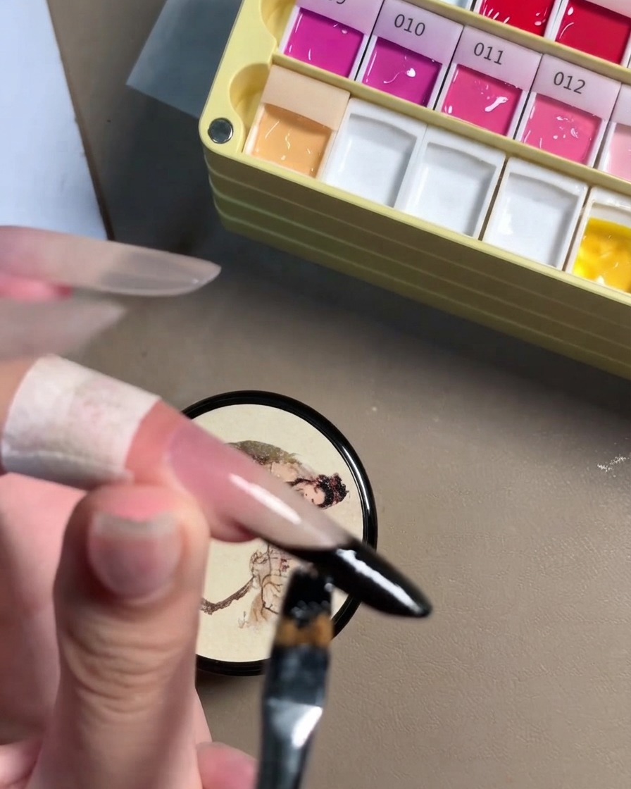 Nahaufnahme eines Detailpinsels, der die schwarze Gellinie an einer Stiletto-Nagelkante perfektioniert.