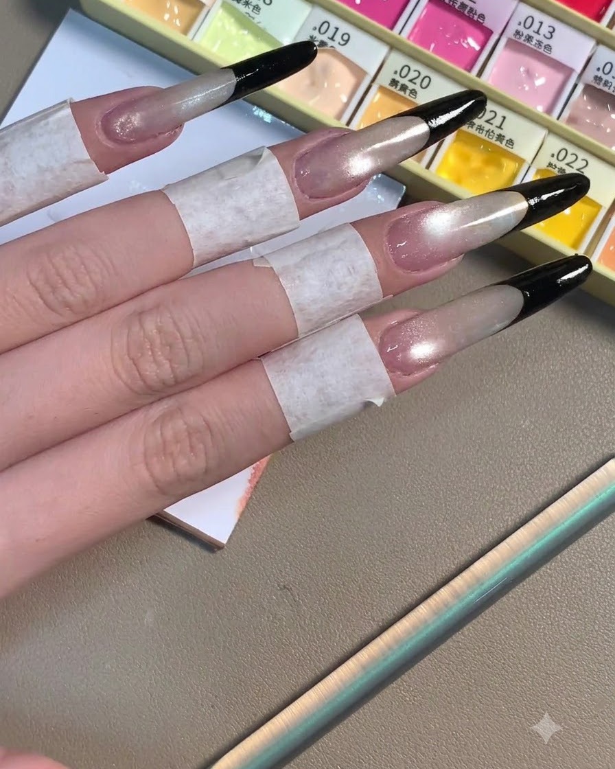 Vier lange Stiletto-Nägel mit vollendeten tiefschwarzen French Tips über einer schimmernden grauen Basis.