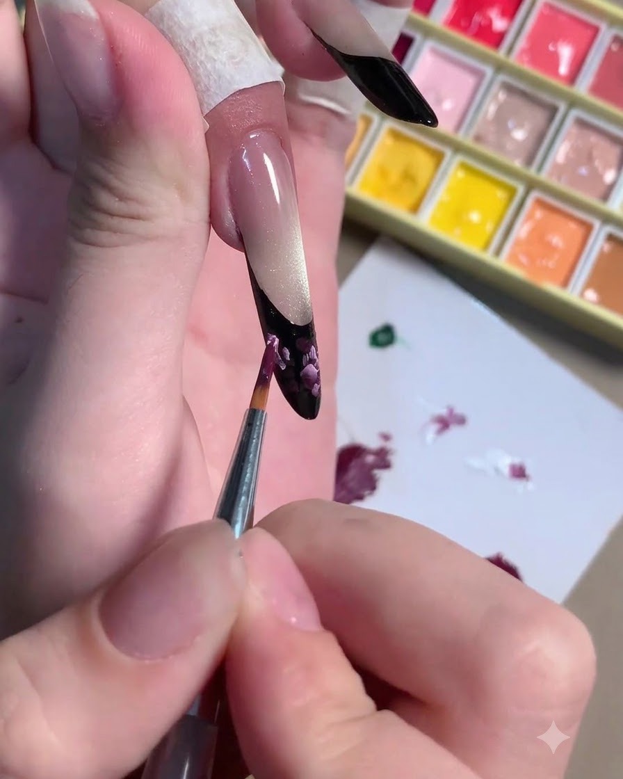Ein feiner Pinsel trägt hellrosa Highlight-Striche über die dunkelviolette florale Nagelkunst auf.