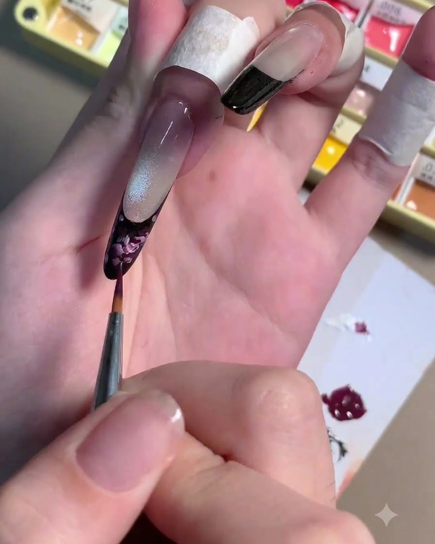 Ein feiner Liner-Pinsel trägt hellrosa Gel-Striche über eine dunkelviolette Rosenbasis auf einem Fingernagel auf.