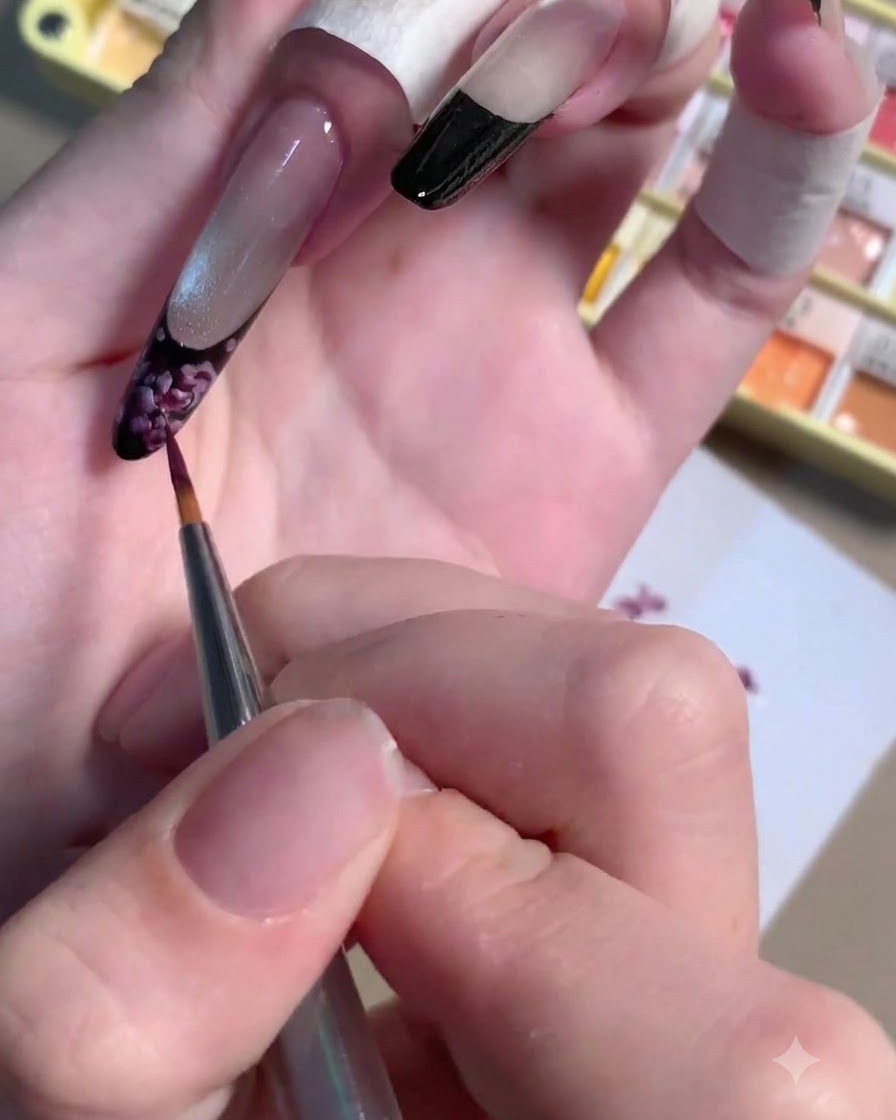 Ein dünner Liner-Pinsel trägt einen kleinen Tropfen dunkelviolettes Gel auf das Zentrum einer gemalten Rose auf.