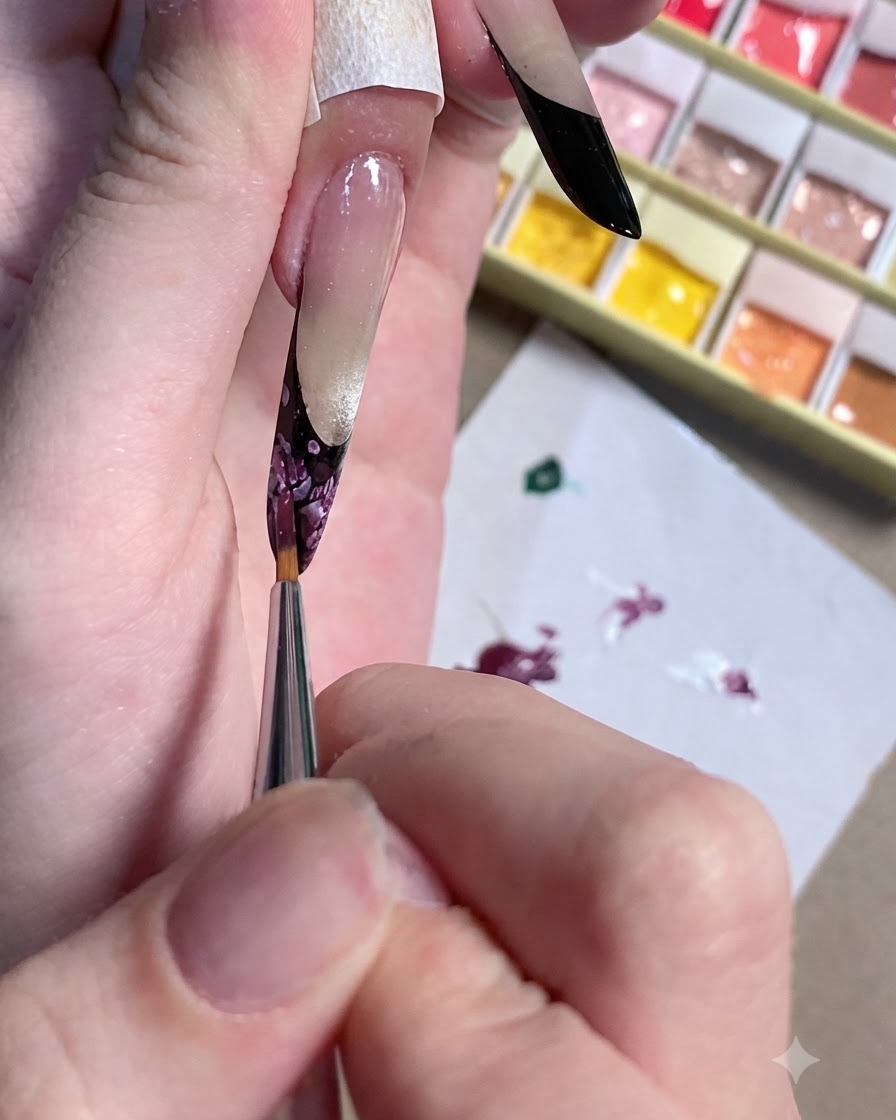 Nahaufnahme eines Detailpinsels, der das dunkle Zentrum eines floralen Nageldesigns verfeinert.