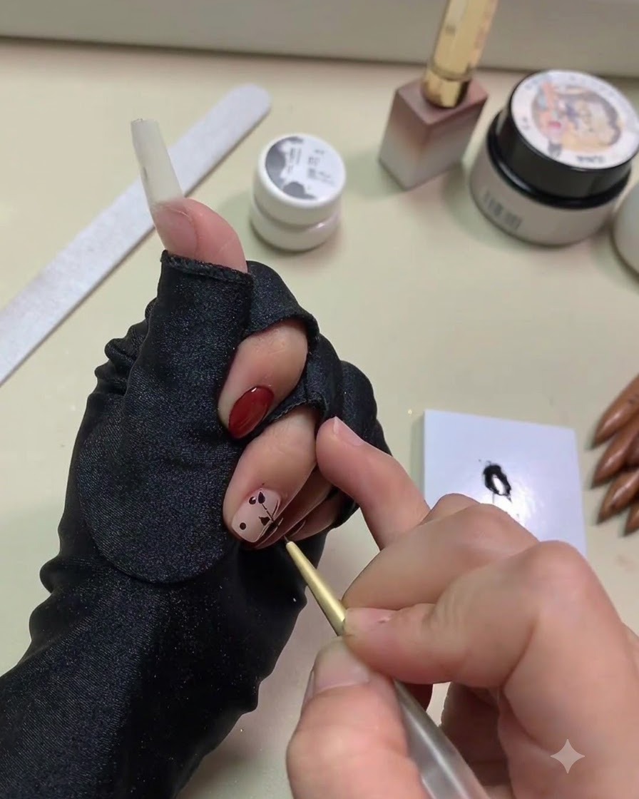 Nahaufnahme einer Hand, die mit einem feinen goldenen Liner-Pinsel schwarzes Gel aus Punkten zu Blattformen auf einer Nude-Basis zieht.
