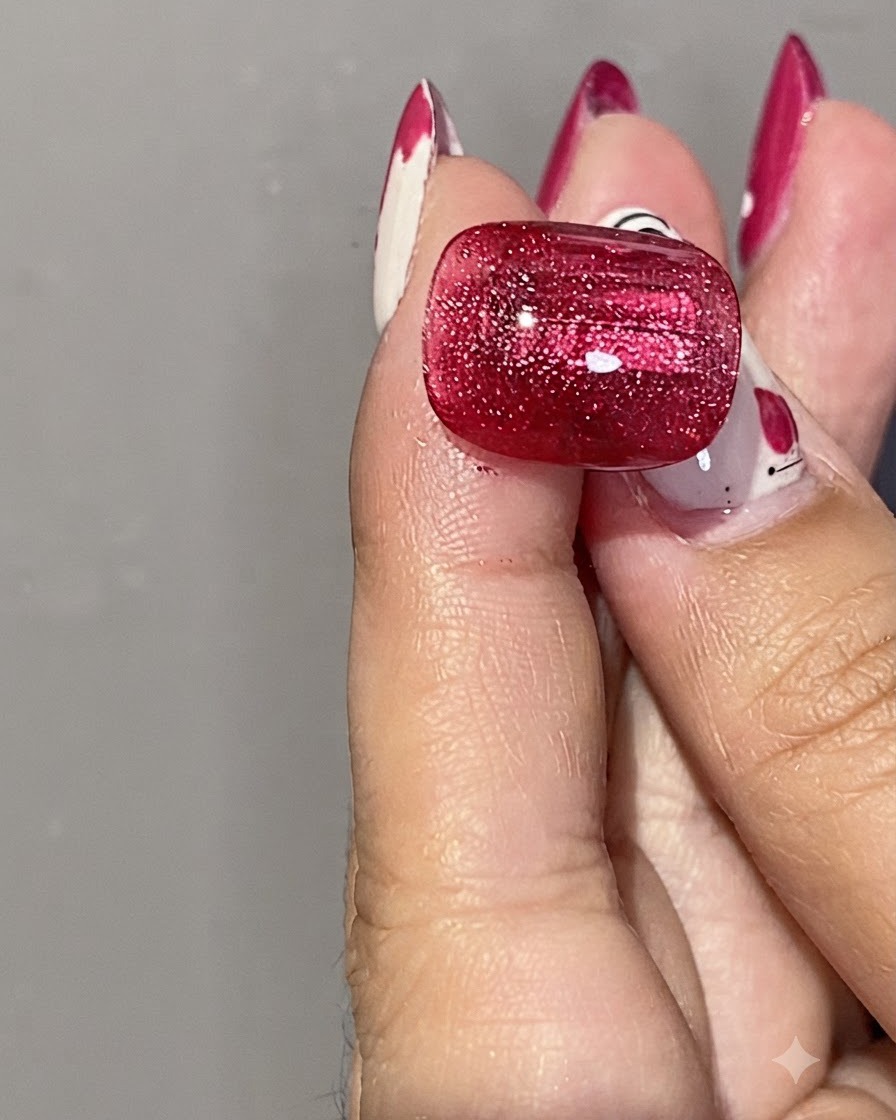 Nahaufnahme einer Hand, die einen zylindrischen Silbermagneten nahe an einen glänzenden roten Cat-Eye-Gel-Nagel hält, um den Schimmer zu formen.