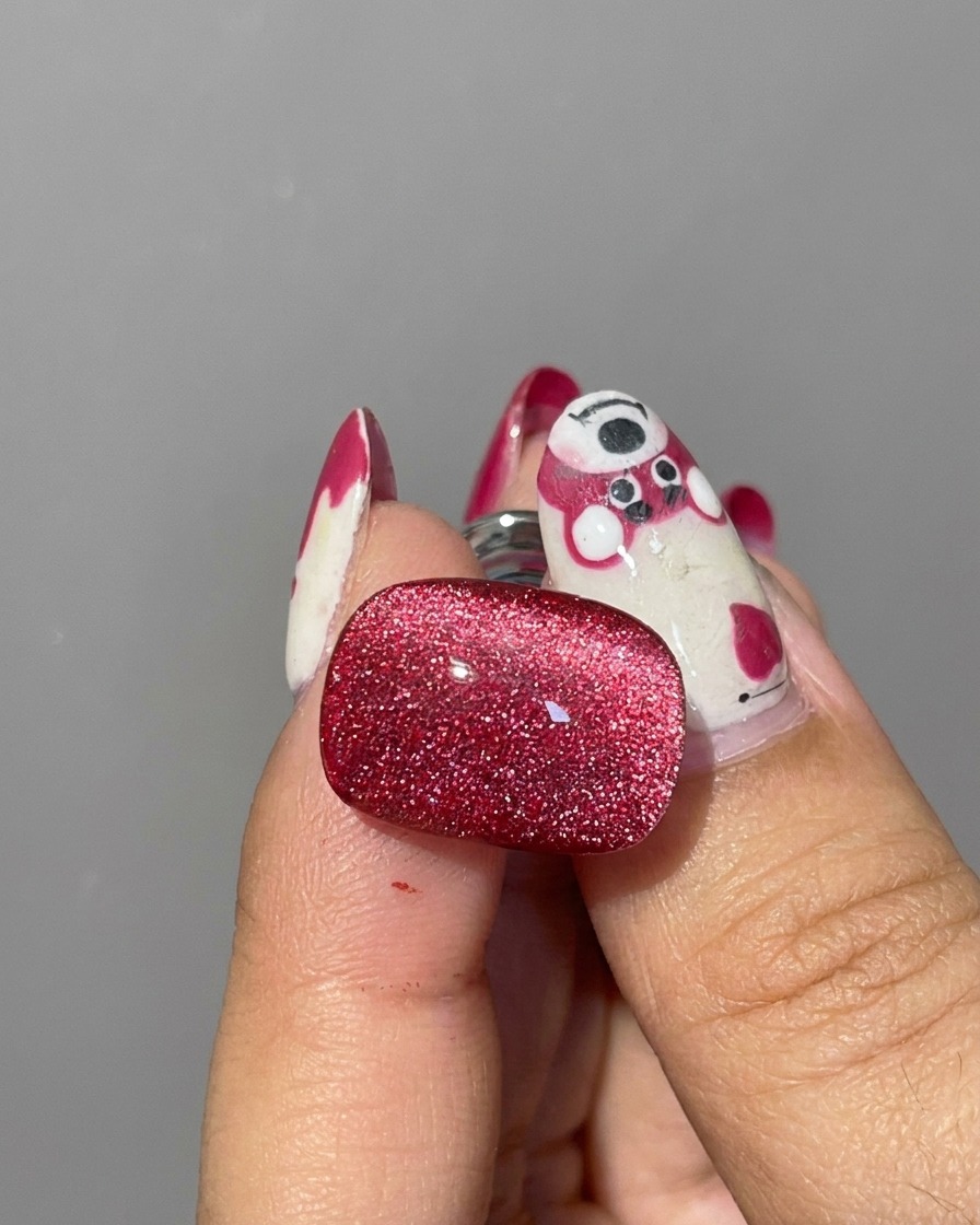 Nahaufnahme eines zylindrischen Silbermagneten, der nahe an die Ränder eines feuchten roten Cat-Eye-Gel-Nagels gehalten wird, um die Glitzerpartikel zu verschieben.