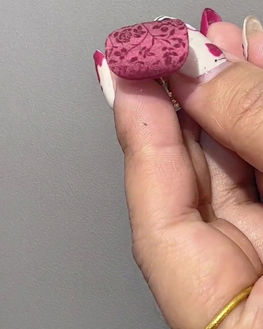 Nahaufnahme eines manikürten Nagels mit einem übertragenen roten Blumenmuster auf einer ungehärteten Glanzbasis.