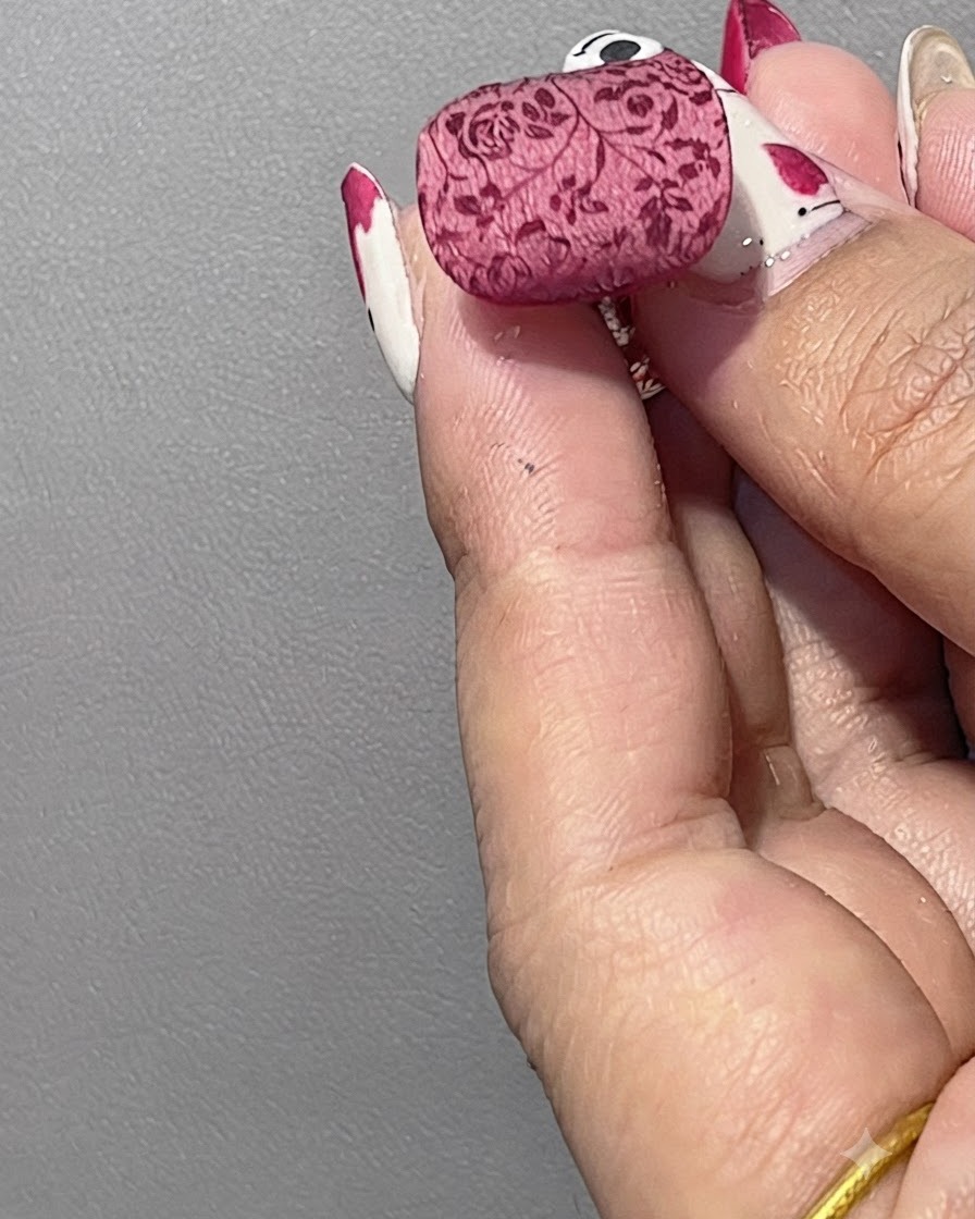 Ein flauschiger Pinsel fegt überschüssiges weißes Puder von einem fertigen Nagel ab, der ein weiches, nebliges Blumenmuster zeigt.