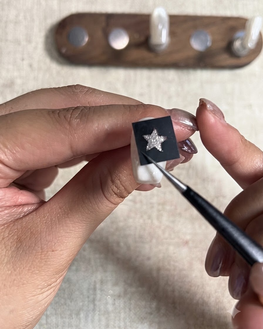 Ein spitzes Werkzeug drückt fest auf einen schwarzen Stern-Schablonenaufkleber, der auf einem lackierten Nageltip platziert ist.