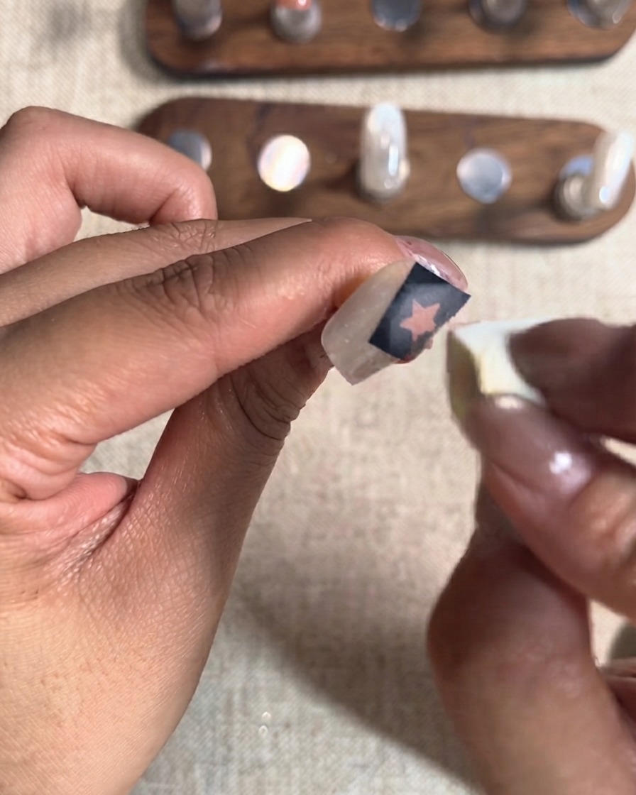 Ein kleiner Kosmetikschwamm tupft eine zweite Schicht rotes Gel über einen Sternausschnitt-Aufkleber auf einem Fingernagel.