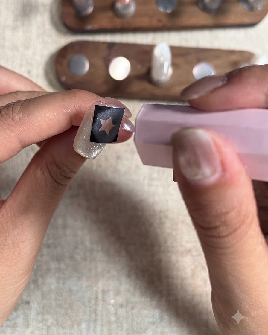 Eine pinke Mini-UV/LED-Härtungslampe wird über einen Fingernagel mit einer Sternschablone gehalten, um die letzte Schicht rotes Gel zu fixieren.