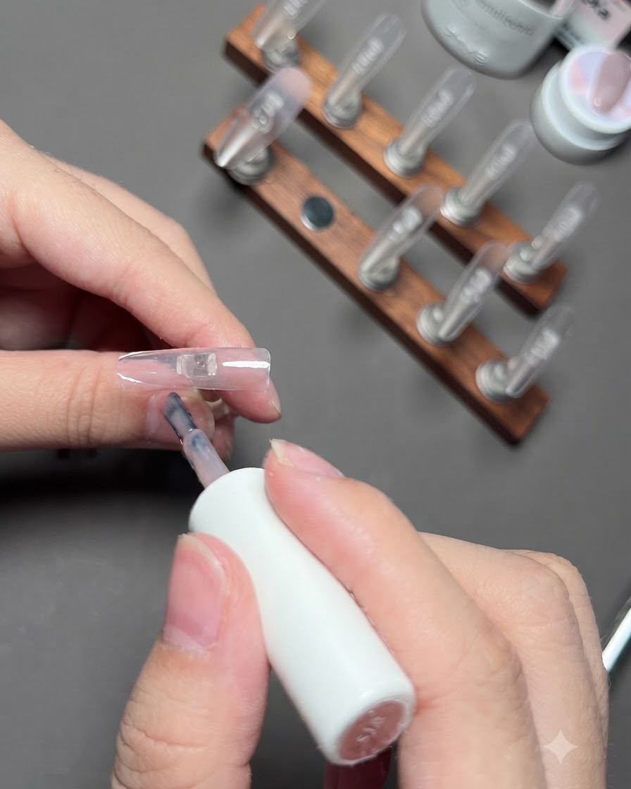 Ein Pinsel trägt Nude-Farbgel auf den Ringfingernagel auf.