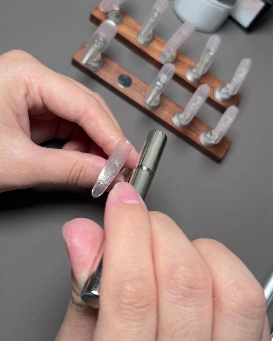 Ein Magnetstab schwebt in der Nähe eines Nagels, um die reflektierenden Cat-Eye-Partikel zu sammeln und zu formen.