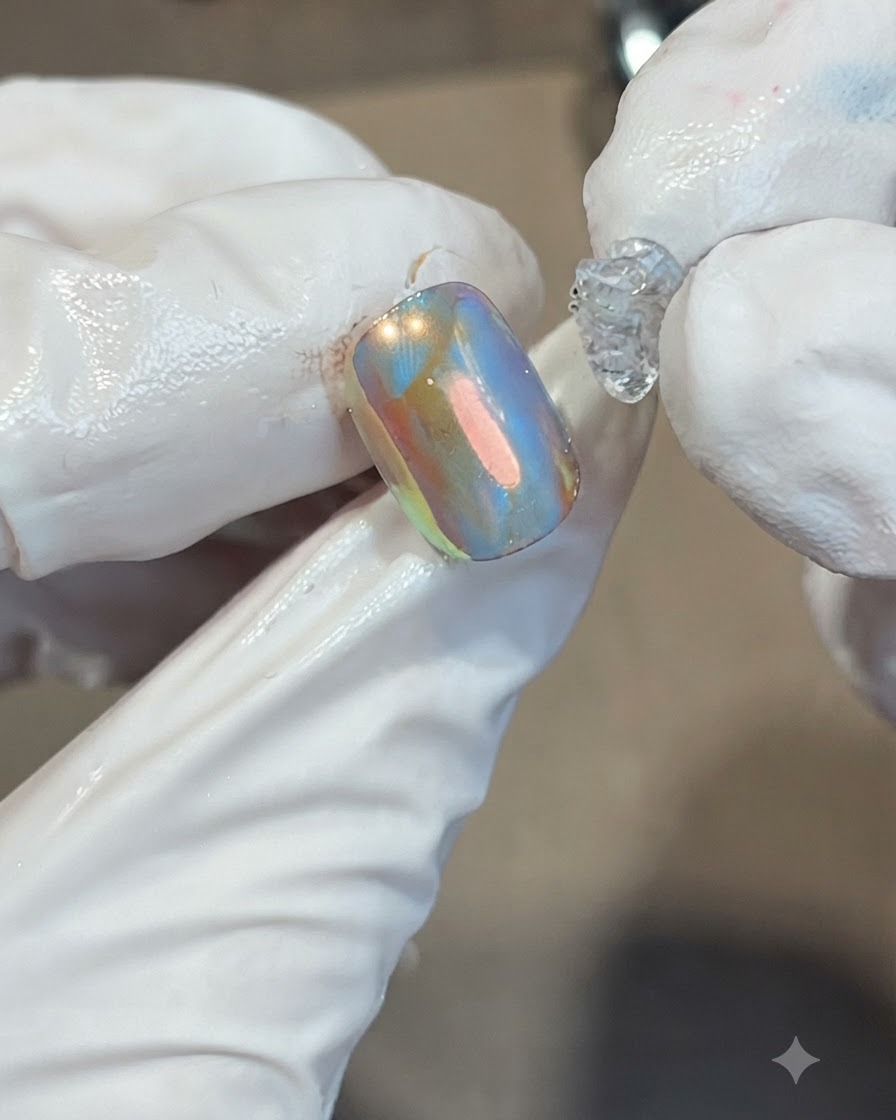 Ein kleiner Klecks dicken, klaren Soft-Candy-Gels wird in der Mitte eines irisierenden orange-blauen Nagels platziert.