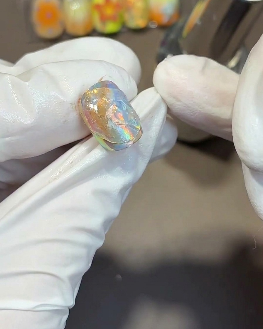 Ein Metallwerkzeug drückt fließende, wellenförmige Texturen in das dicke, klare Gel auf einem irisierenden Nagel.