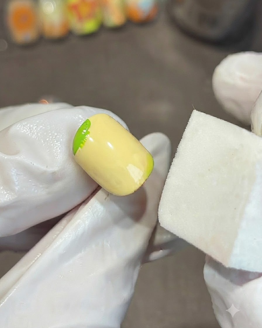 Ein Schwammblock neben einem gelben Nagel verblendet einen grünen Gel-Farbverlauf an der Ecke.