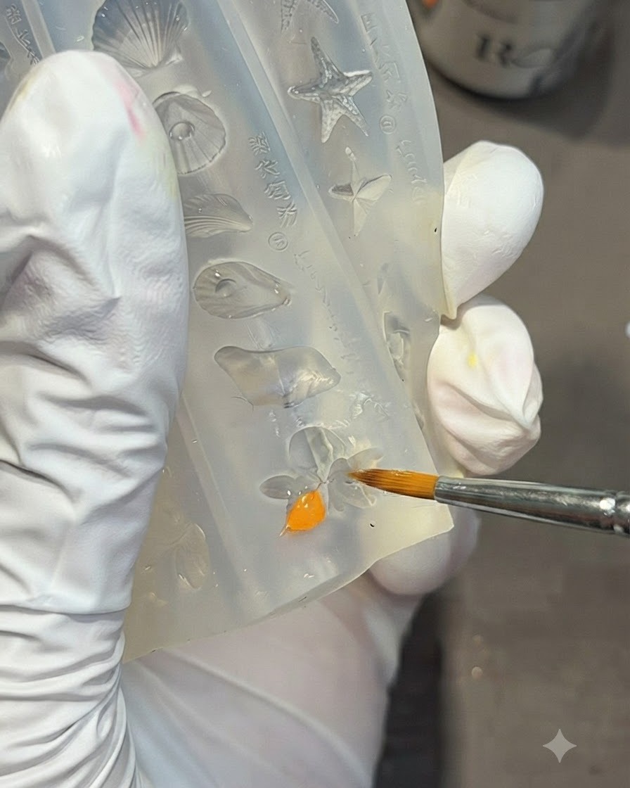 Ein Detailpinsel füllt eine Lilienblütenform in einer klaren Silikonform mit leuchtend orangenem Gel.