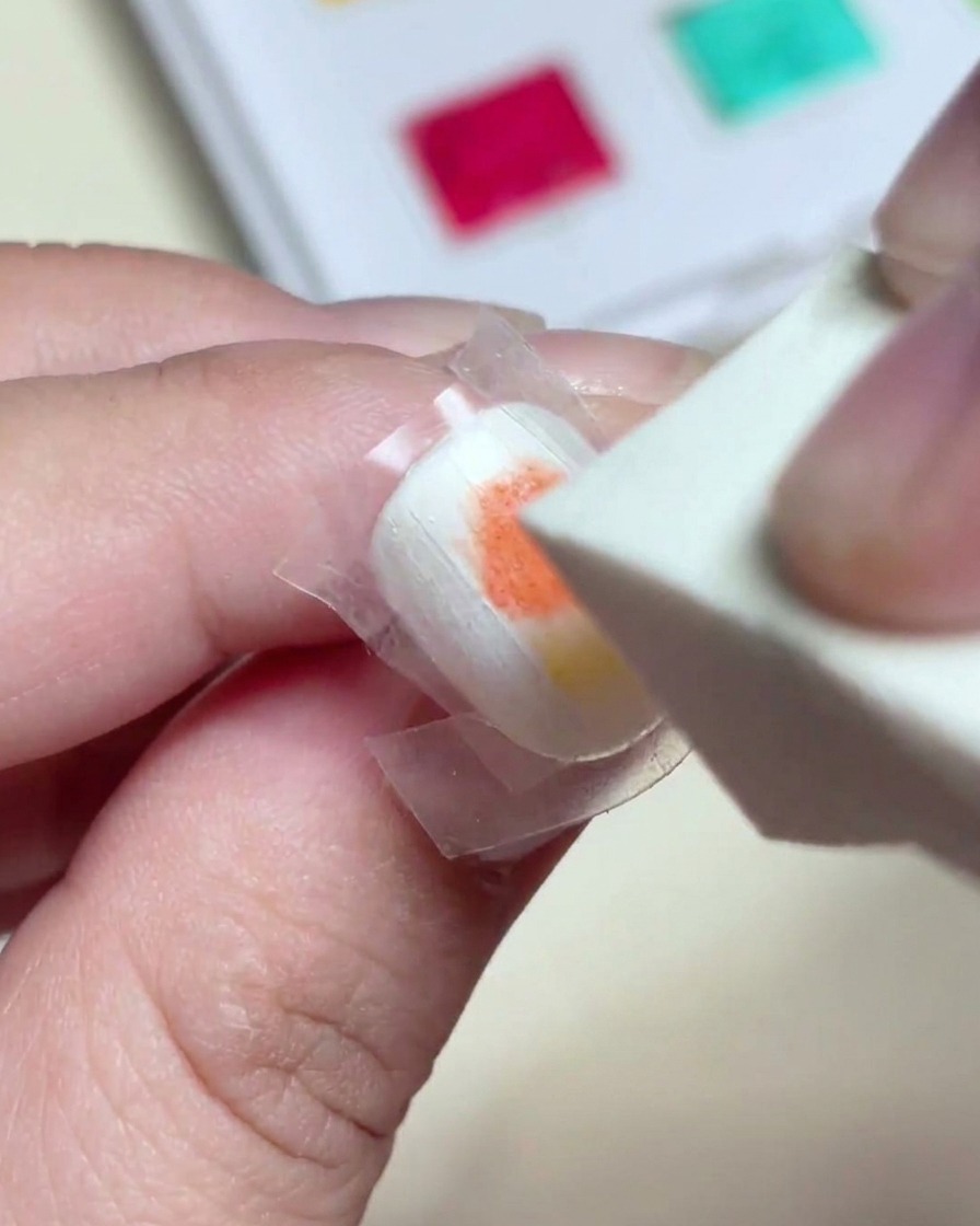 Ein Make-up-Schwamm tupft sanft über nasses rotes und gelbes Farbgel, um einen nahtlosen Farbverlauf auf dem Nagel zu erzeugen.