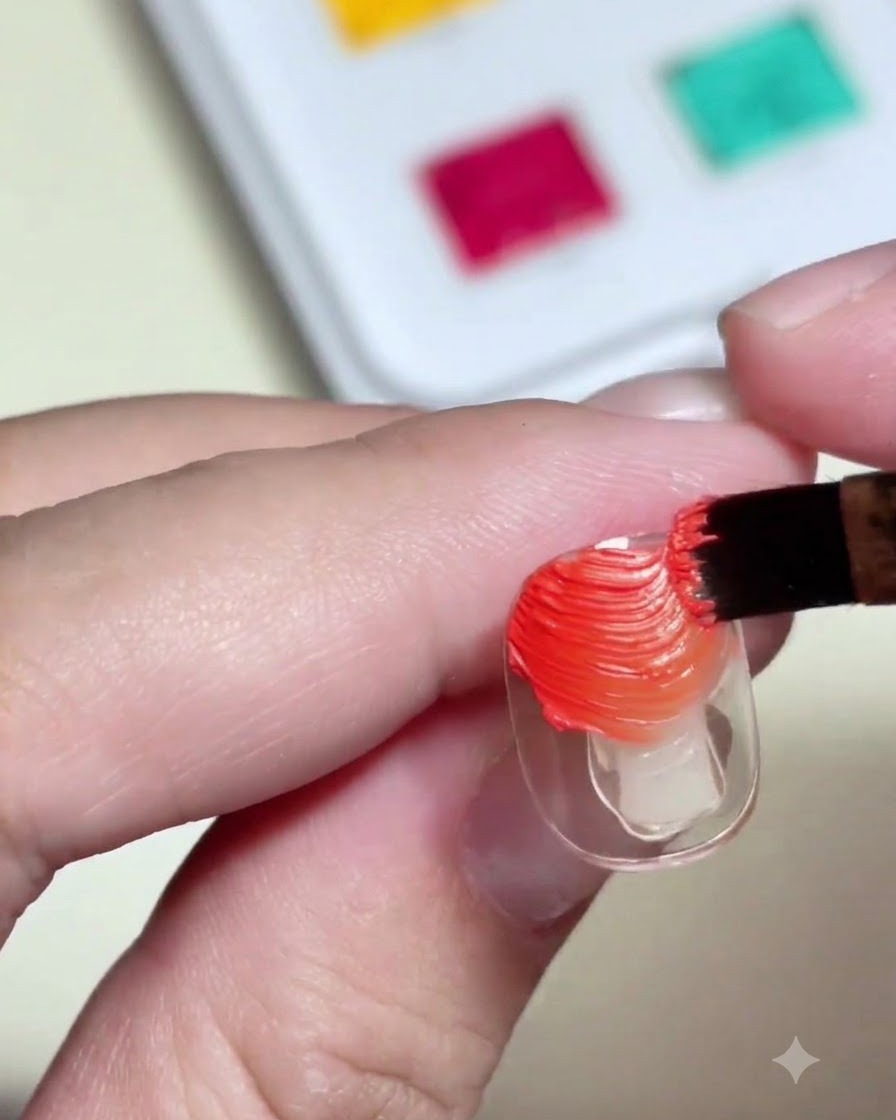 Ein Nagelpinsel trägt strukturiertes, orange- und gelbfarbenes Painting-Gel auf eine durchsichtige Nagelspitze auf.