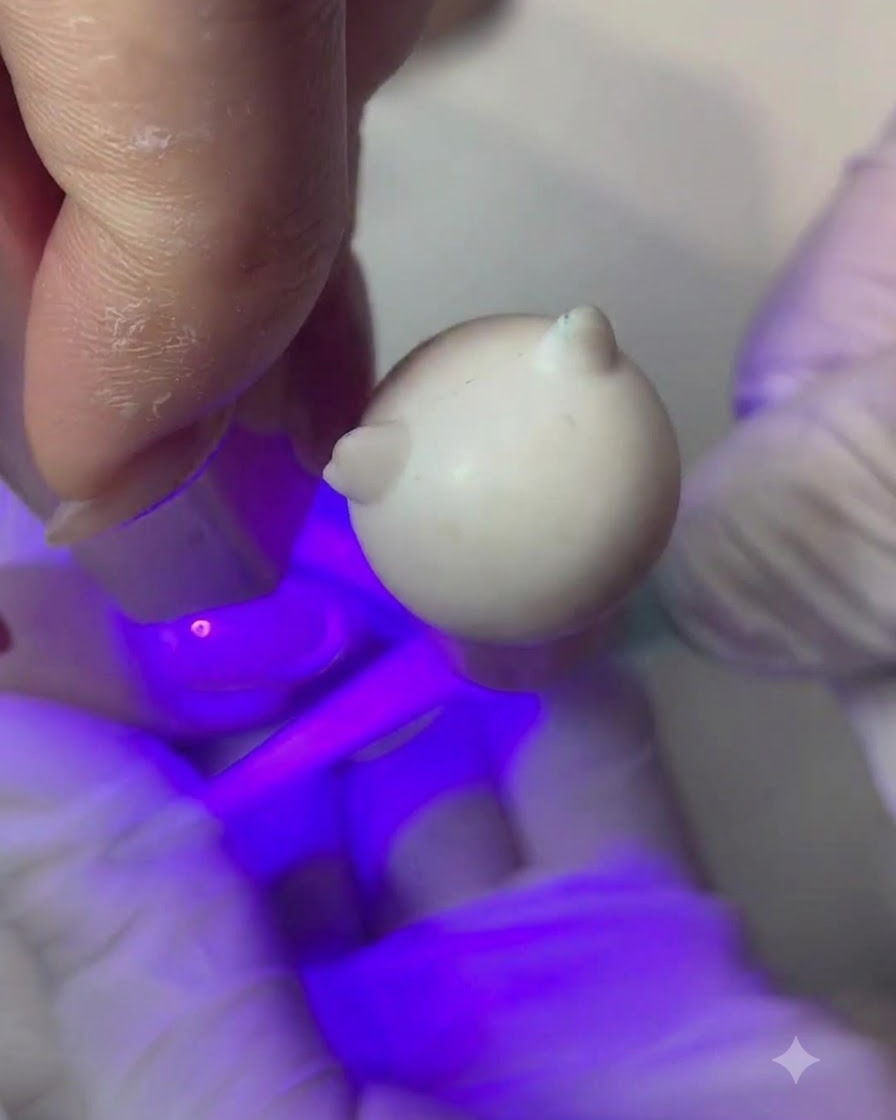 Ein feiner Pinsel trägt eine dünne Schicht Nude-Pfirsich-Farbgel auf einen Fingernagel auf.