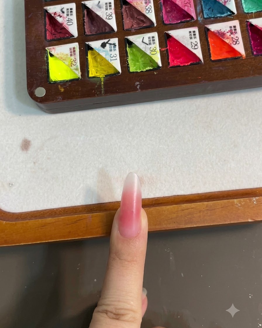Ein Fingernagel mit rosa Blush-Verlauf unter einer UV-Lampe zum Aushärten.