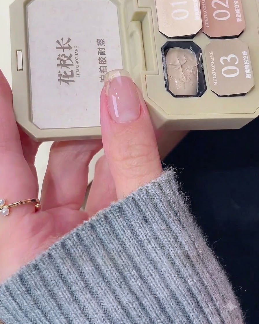 Eine Nahaufnahme eines natürlichen Fingernagels, auf den in der Nähe der Nagelspitze ein weißer Basislack aufgetragen wird.