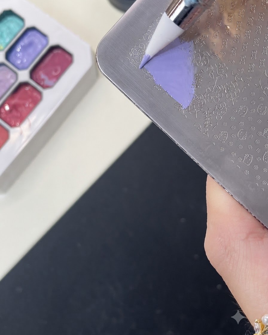 Ein Pinsel trägt lila Farbgel über ein eingraviertes Hello Kitty Muster auf einer Metall-Stamping-Platte auf.