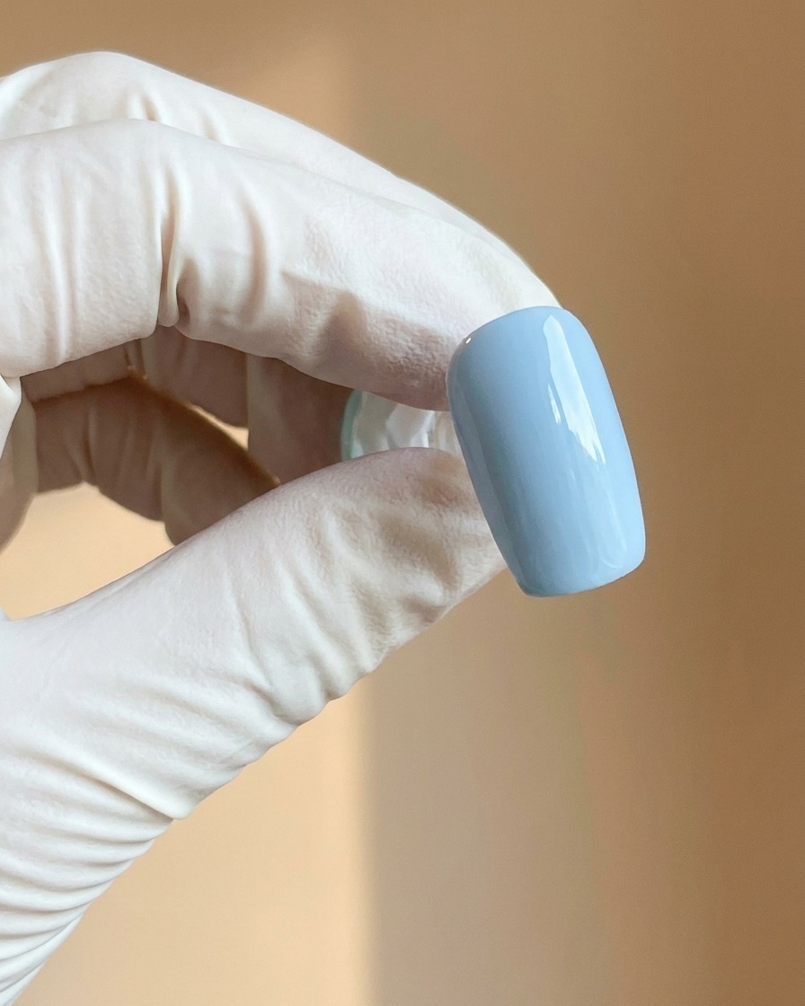 Eine behandschuhte Hand hält einen hellblauen Nagel mit einer glatten, matten Oberfläche.