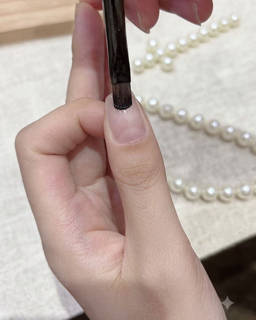 Ein flacher Gelnadelpinsel trägt schwarzen Gellack auf die Nagelspitze eines natürlichen Fingernagels auf.
