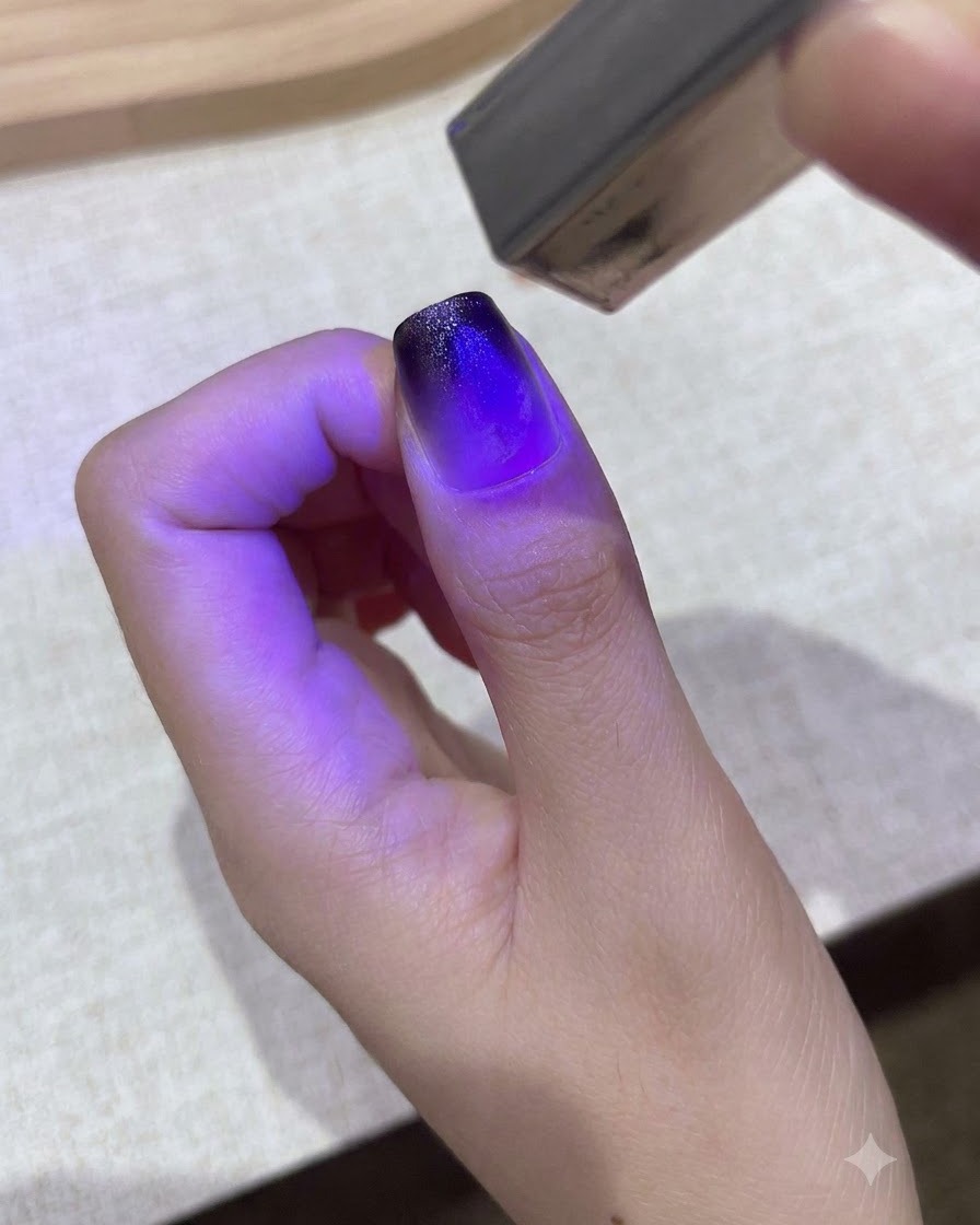 Eine kleine lila Handheld-UV/LED-Lampe härtet ein Farbverlaufs-Gel-Design auf einem Daumennagel aus.