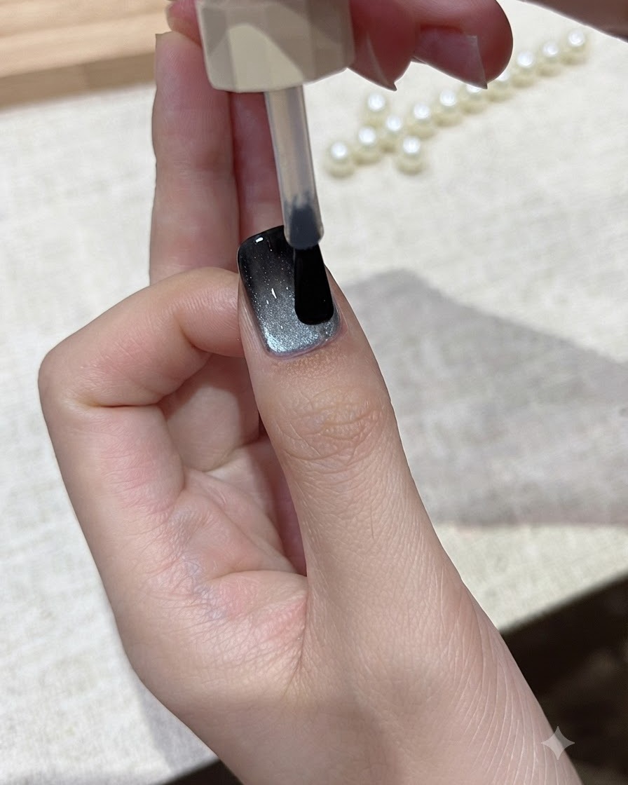Ein Pinsel lässt eine Schicht klaren Glanzüberlack über das fertige Cat-Eye-Nageldesign gleiten.