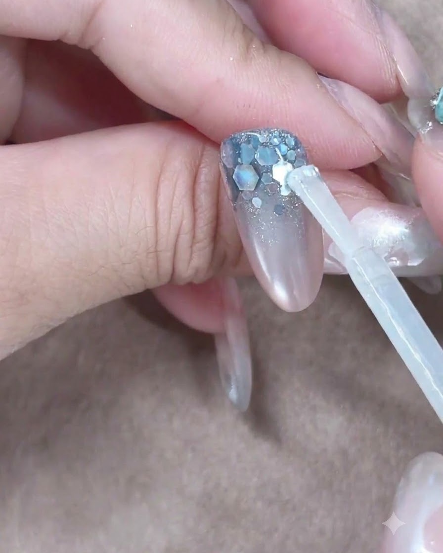 Ein Aufbaugel-Pinsel platziert einen klaren Tropfen nahe der Nagelhaut, der den Nagel hinabfließt.