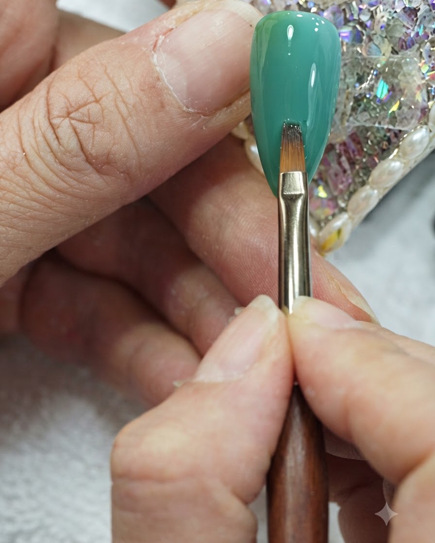Ein flacher Nail-Art-Pinsel führt sanfte vertikale Striche über die Mitte eines grün-petrolfarbenen Gradienten-Nagels aus.