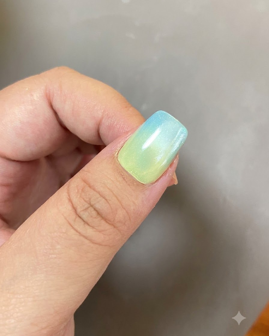 Eine fertige Gel-Maniküre mit Blau-Gelb-Farbverlauf und leuchtendem Ring-Design unter weichem Licht.