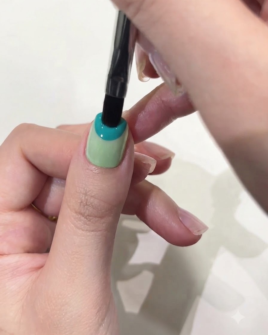 Nahaufnahme eines flachen Gelpinsels, der pastellblaues Solid Gel auf die obere Hälfte eines Daumennagels aufträgt.
