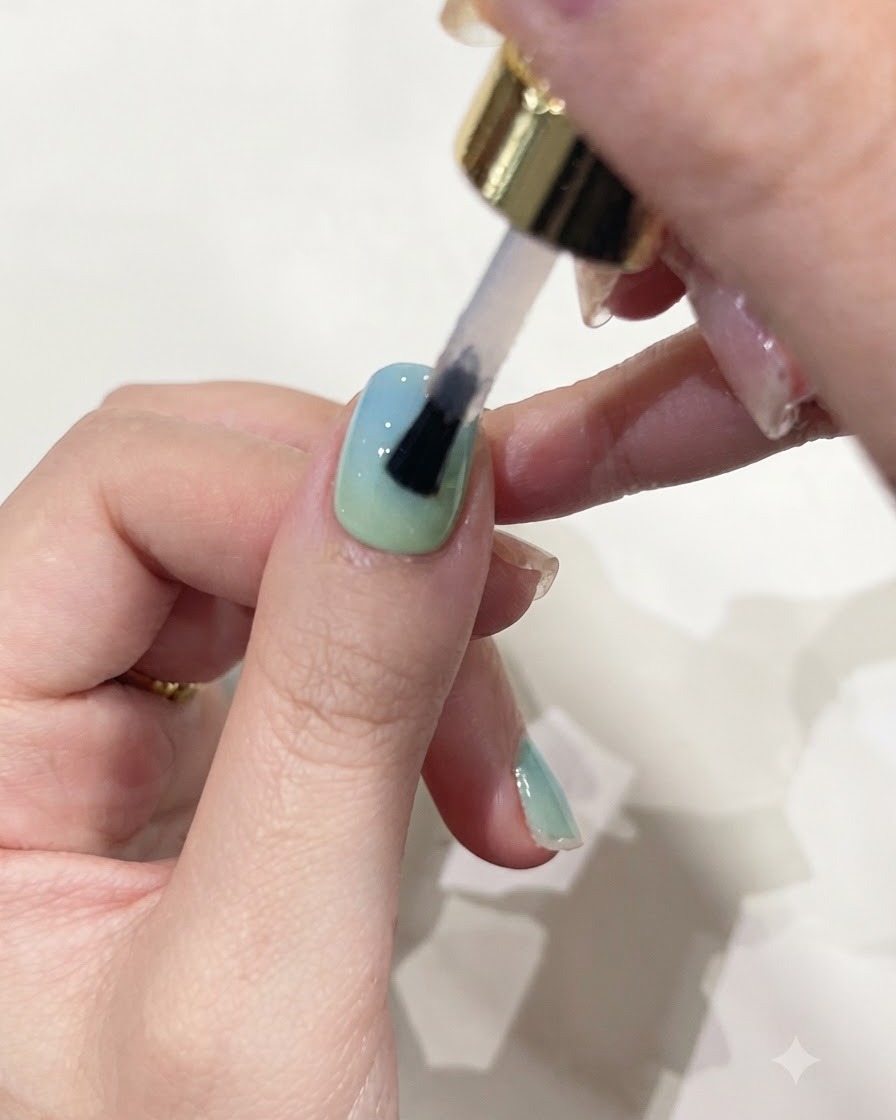 Ein Pinsel trägt klares Aufbaugel auf einen Fingernagel mit Farbverlauf auf.